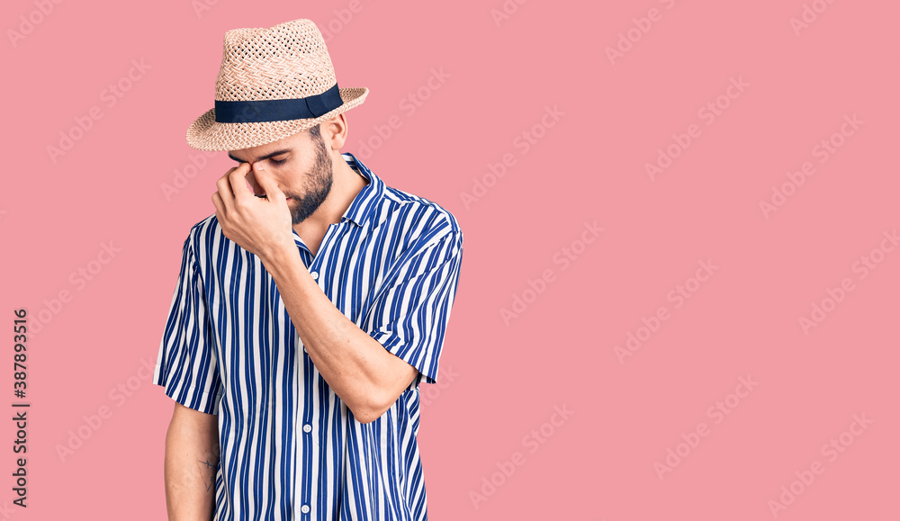 Young handsome man with beard wearing summer hat and striped shirt tired rubbing nose and eyes feeling fatigue and headache. stress and frustration concept. Young handsome man with beard wearing summer hat and striped shirt tired rubbing nose and eyes feeling fatigue and headache. stress and frustration concept.