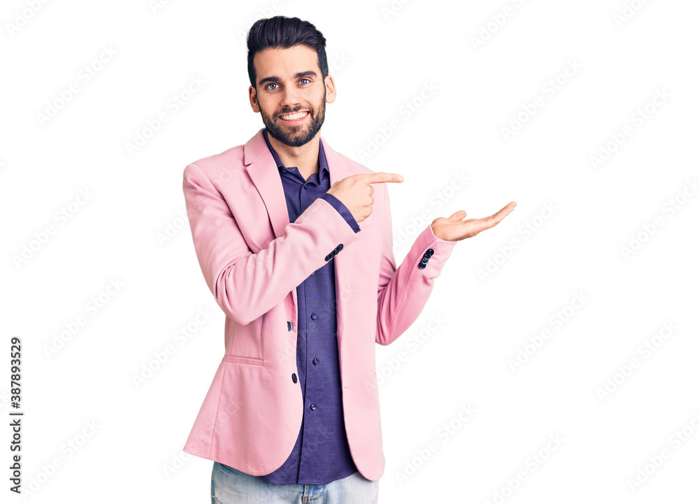 Young handsome man with beard wearing elegant jacket amazed and smiling to the camera while presenting with hand and pointing with finger. Young handsome man with beard wearing elegant jacket amazed and smiling to the camera while presenting with hand and pointing with finger.