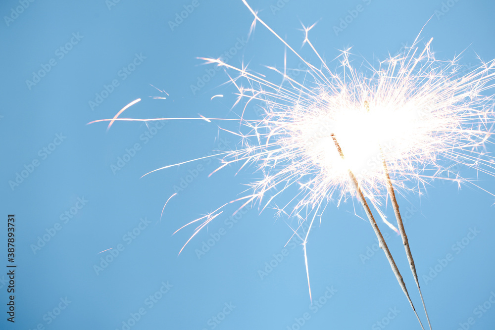 Fototapeta Bright burning sparklers on light blue background, closeup