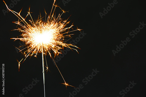 Bright burning sparkler on black background, closeup. Space for text