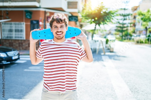 Fotografie Young caucasian skater man smiling happy holding skate walking at street of city