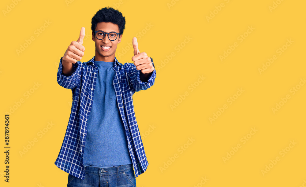 Young african american man wearing casual clothes and glasses approving doing positive gesture with hand, thumbs up smiling and happy for success. winner gesture. Young african american man wearing casual clothes and glasses approving doing positive gesture with hand, thumbs up smiling and happy for success. winner gesture.