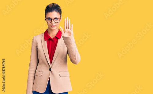 Young beautiful woman wearing business shirt and glasses doing stop sing with palm of the hand. warning expression with negative and serious gesture on the face. photo