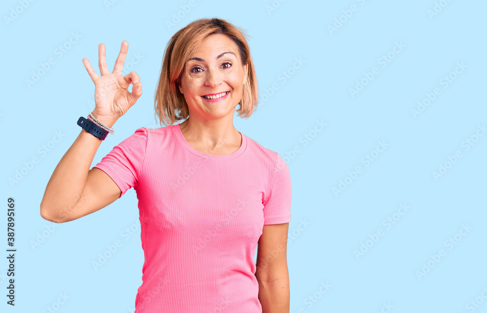 Young blonde woman wearing sportswear smiling positive doing ok sign with hand and fingers. successful expression. Young blonde woman wearing sportswear smiling positive doing ok sign with hand and fingers. successful expression.