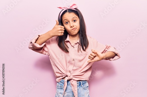 Beautiful child girl wearing casual clothes doing thumbs up and down, disagreement and agreement expression. crazy conflict