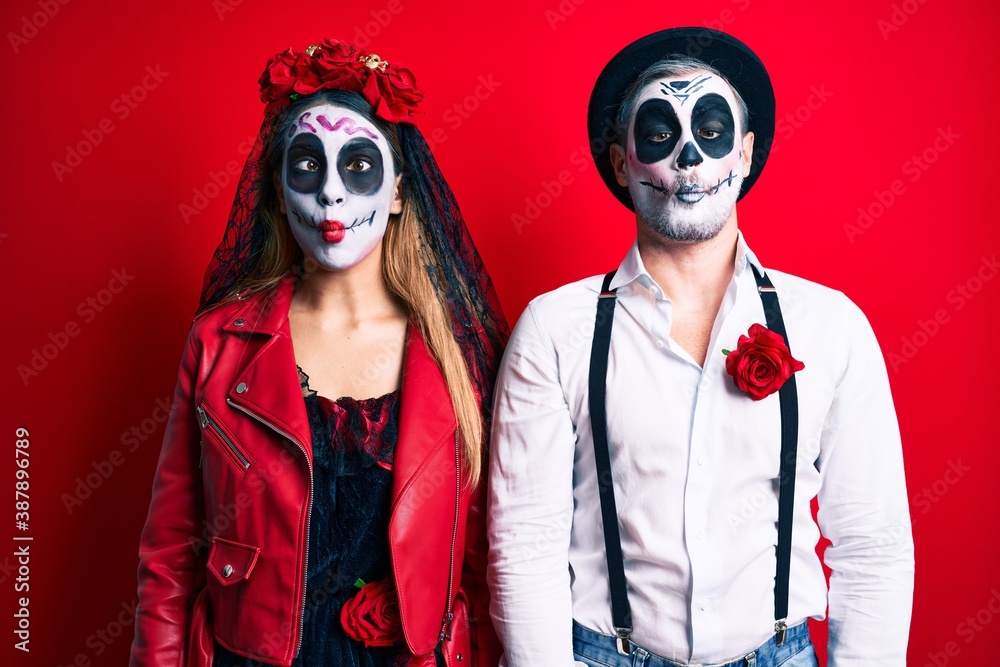 Couple wearing day of the dead costume over red making fish face with lips, crazy and comical gesture. funny expression. Couple wearing day of the dead costume over red making fish face with lips, crazy and comical gesture. funny expression.