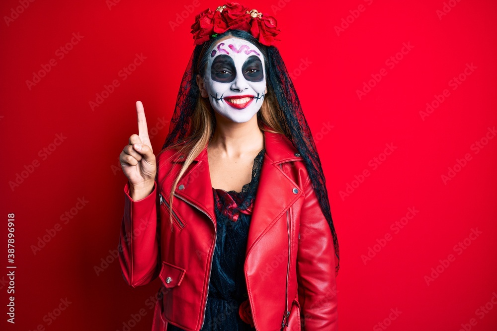Woman wearing day of the dead costume over red showing and pointing up with finger number one while smiling confident and happy.