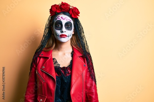 Woman wearing day of the dead costume over yellow with serious expression on face. simple and natural looking at the camera.