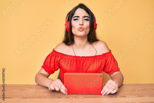 Brunette teenager girl using touchpad wearing headphones looking at the camera blowing a kiss being lovely and sexy. love expression.