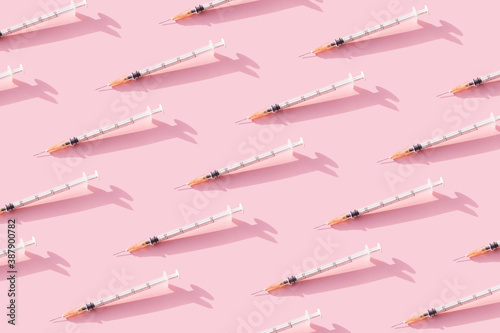 Creative medicinal pattern from syringes of pink background. Colorful concept of New Corona virus 2019-nCoV or COVID-19 vaccine. Flat lay, top view.