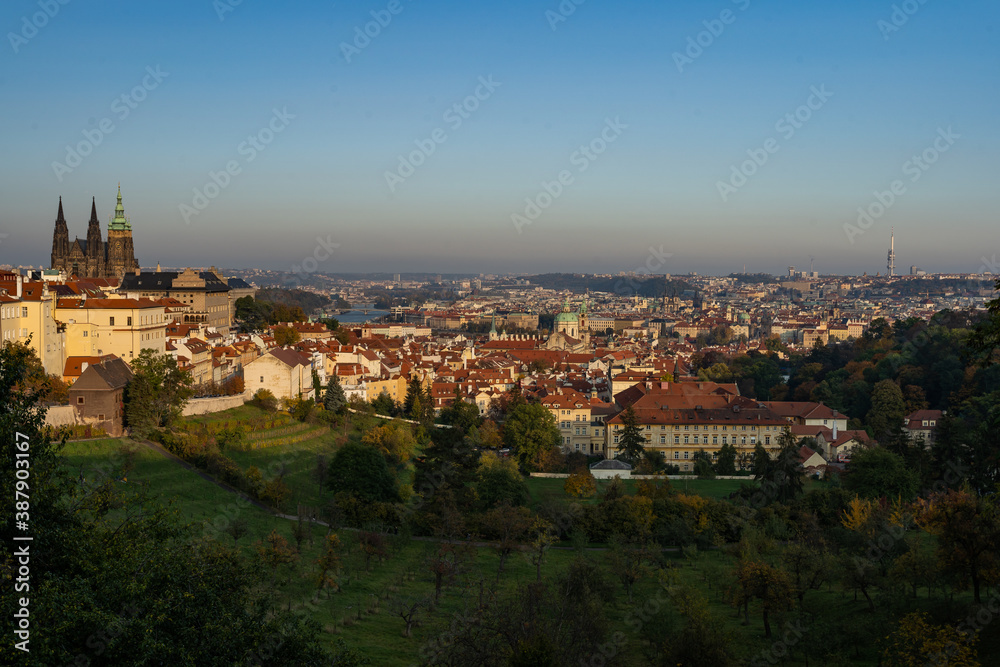 the old St. Vitus Cathedral and Prague Castle and the nearby ones with trees and grass in autumn   and a sky without clouds at sunset in the center of city