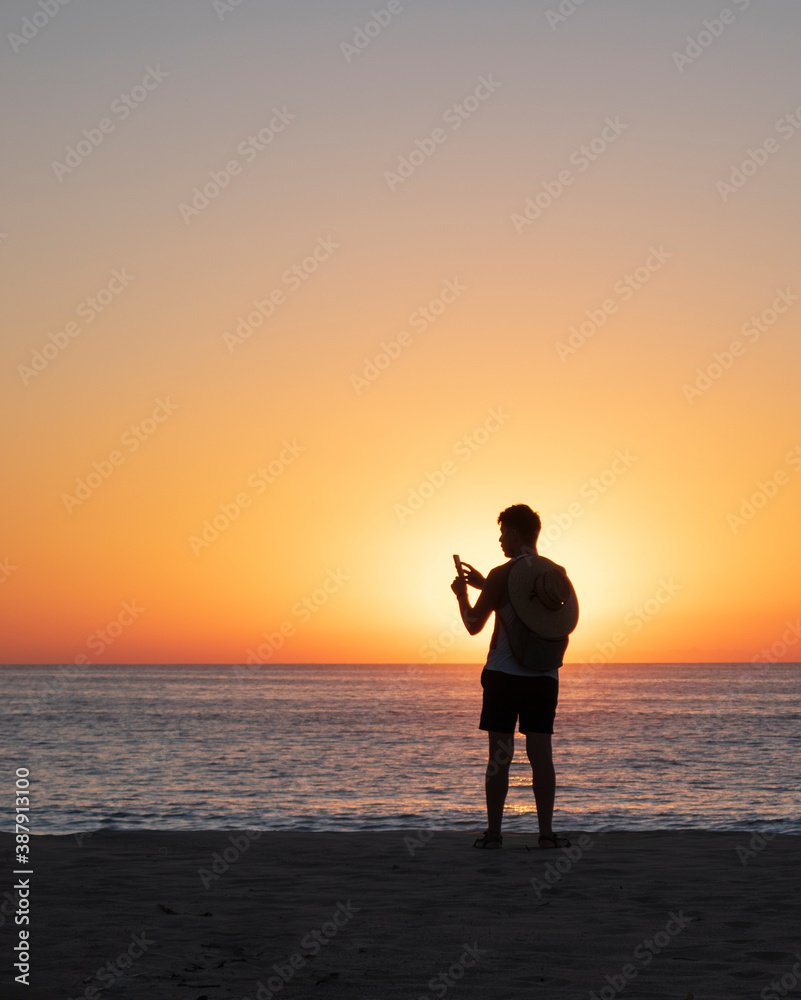 Man silhouette in a beautiful beach while taking a photo with his cellphone
