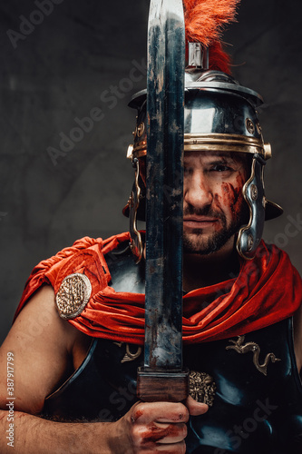 Serious military roman with dark armour and helmet posing using his sword in dark background Fototapeta