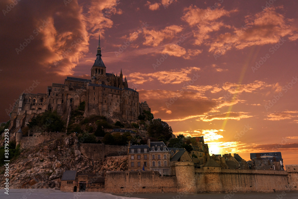 The medieval abbey, cathedral, and hamlet of Mont Saint Michel in France stands high on a hill on the coast of the English Channel during a beautiful sunset.