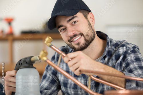 smiling plumber using welding gas torch to solder copper pipes photo