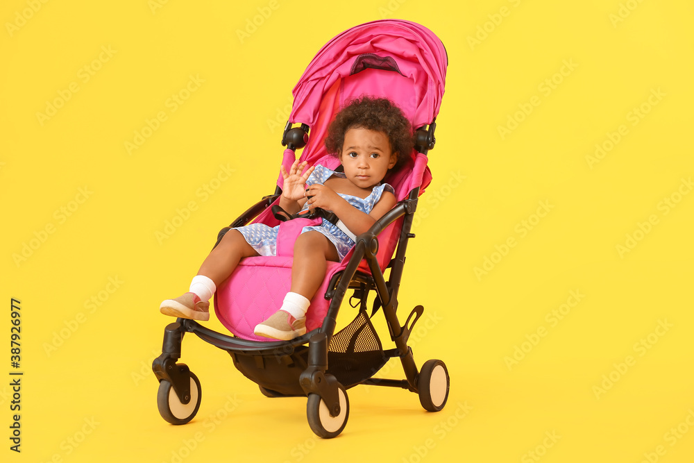 Cute African-American baby in stroller on color background