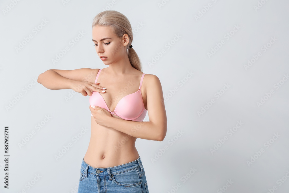 Naklejka premium Young woman checking her breast on grey background. Cancer awareness concept