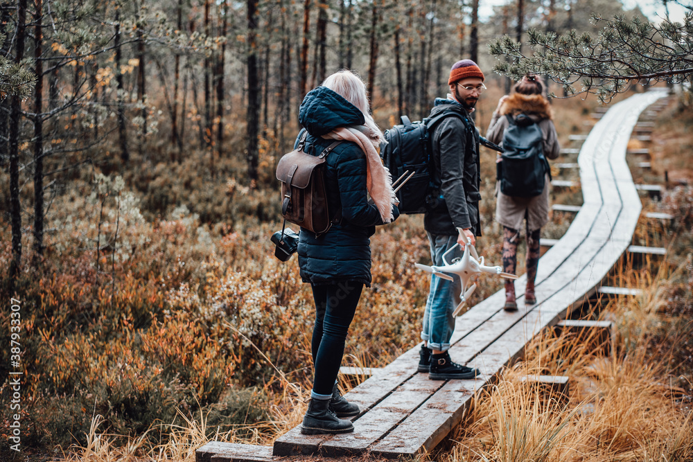 Group of three friends guy and two girls going through wooden path following each other in autumn lovely forest. Group of three friends guy and two girls going through wooden path following each other in autumn lovely forest.