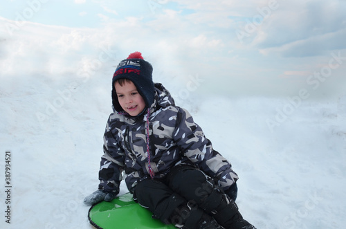 Little boy having fun in the snow. a boy in a winter jacket and hat throws up snow, rides down a hill