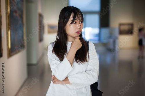 Chinese female visitor looking at artwork painting in the museum indoors