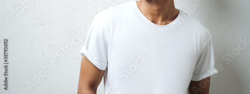 Handsome asian guy in white blank t-shirt, grunge wall, studio portrait. Wide screen, panoramic