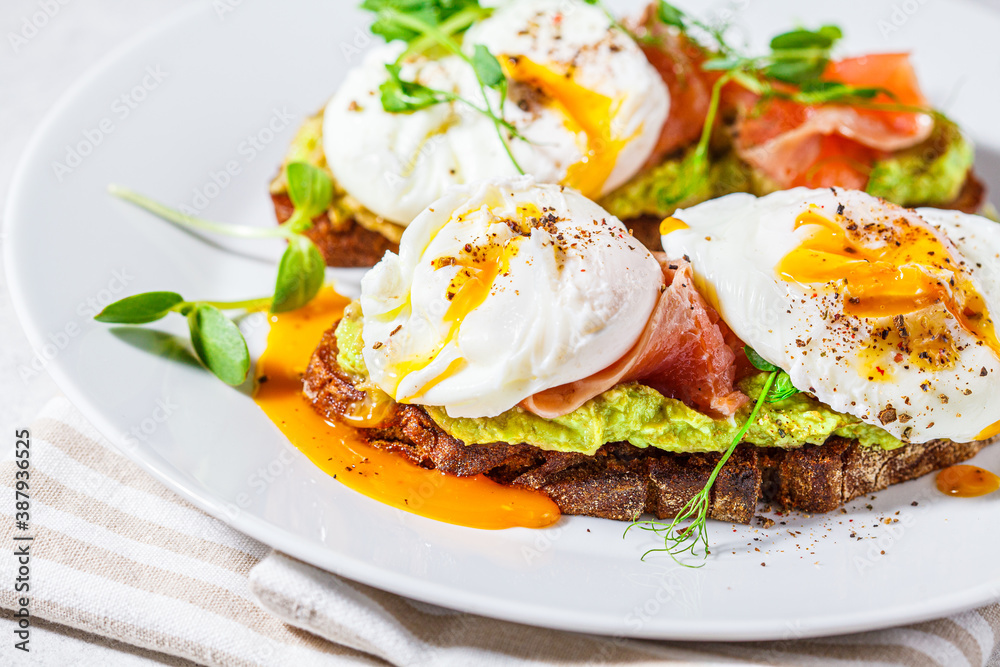Toast with salmon, poached egg and avocado on white plate. Poached egg with salmon and guacamole on rye bread. Toast with salmon, poached egg and avocado on white plate. Poached egg with salmon and guacamole on rye bread.