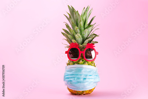 COVID Travel concept. Pineapple in sunglasses and medical mask on a pink background. Pineapple in pink sunglasses and face mask - New normal travel