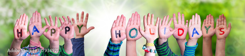 Children Hands Building Colorful English Word Happy Holidays. Sunny Green Grass Meadow As Background