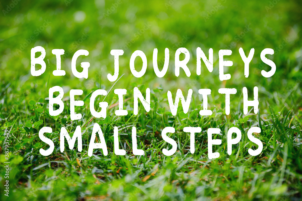 Inspirational quote big journeys begin with small steps on green grass background.