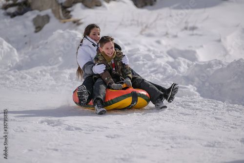 two happy delightful kids boy and girl in ski suit riding down snow hill with pleasure on rubber tube during winter outdoor leisure activity fun