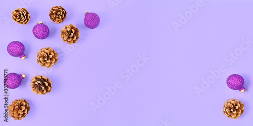 Christmas banner with fir cones and gittering purple tree baubles on light violet background with empty copy space in middle