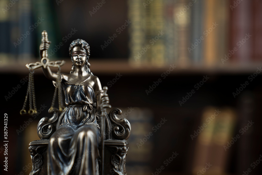 Law and justice concept. Judge chamber. Themis sculpture on brown desk. Collection of legal books in the bookshelf.