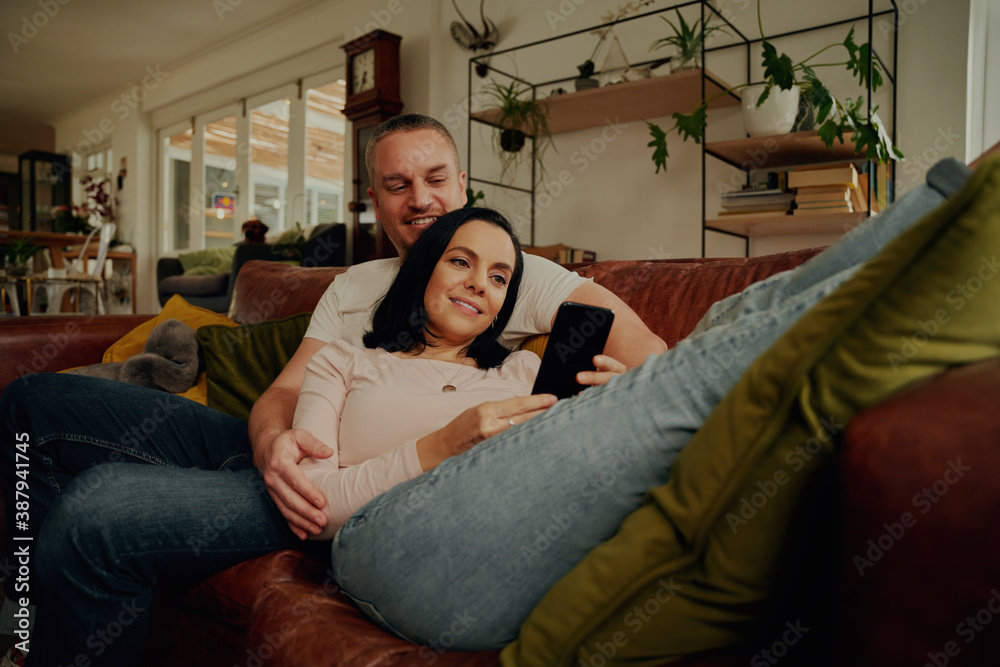 Obraz premium Smiling young woman using phone while relaxing with husband on couch at home