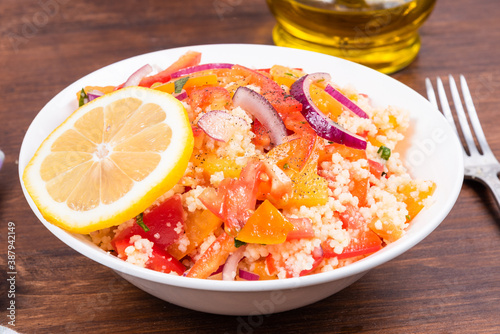 Traditional Mediterranean salad of couscous, tomato, ypeper and onion in a plate on a wooden table - Moroccan and Algerian cuisine