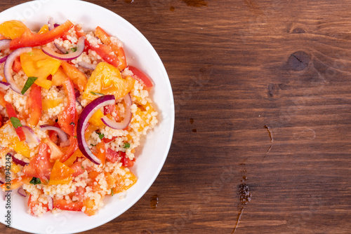 Traditional Mediterranean salad of couscous, tomato, pepper and onion in a plate on a wooden table, close-up, top view, copy space - Moroccan and Algerian cuisine