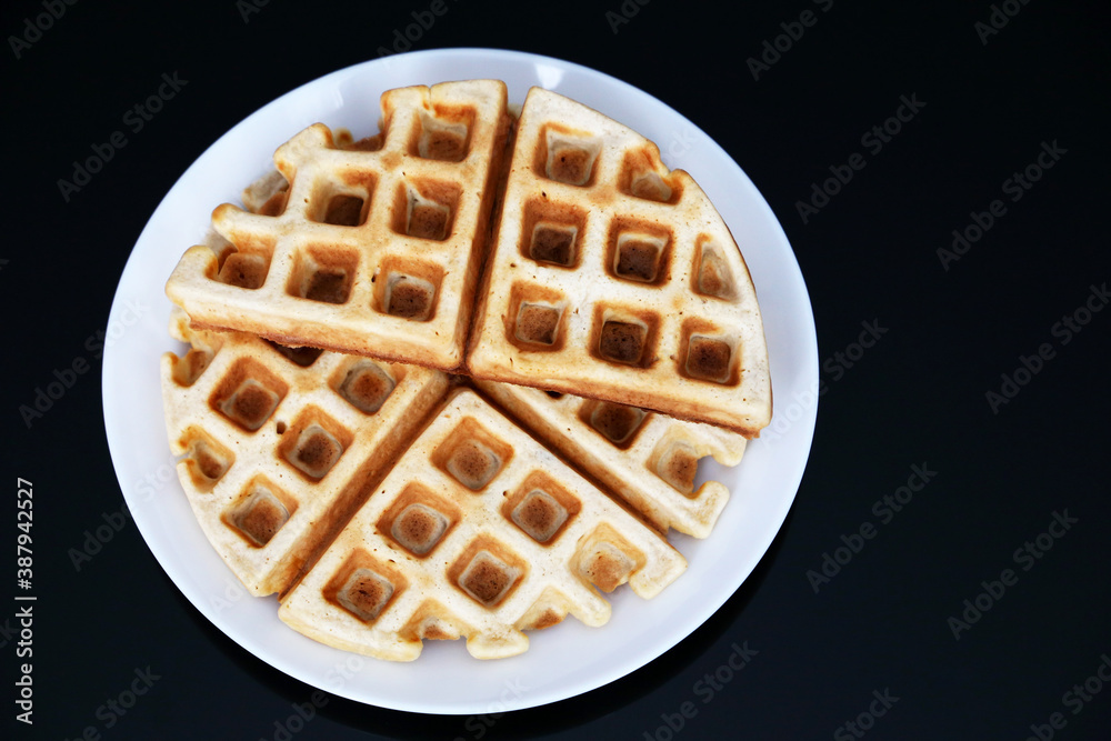Belgian waffles in white plate on black glass table, top view. Healthy breakfast, pieces of freshly baked classic wafer Belgian waffles in white plate on black glass table, top view. Healthy breakfast, pieces of freshly baked classic wafer
