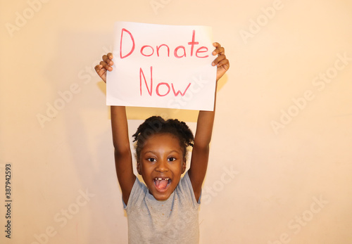 Happy Child Holding a Donate Now Sign up over head white background indoors