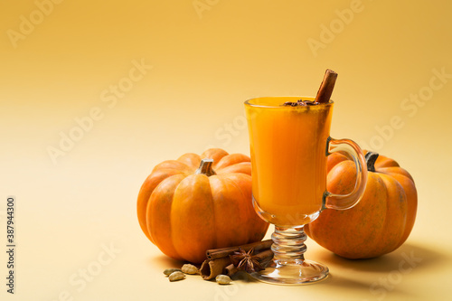 Pumpkins orange coctail drink in glass on yellow background
