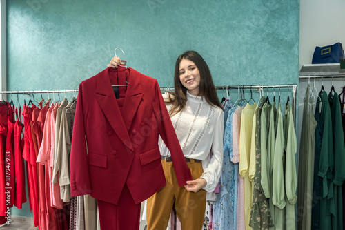 Attractive woman choosing stylish jacket or dress in clothing store