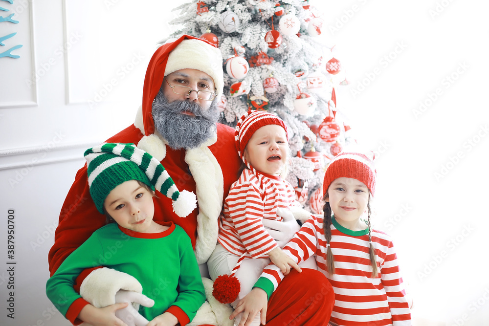 Fototapeta premium Santa Claus sitting with little cute elves over Christmas background. Time of miracles. Gifts from Santa Claus.