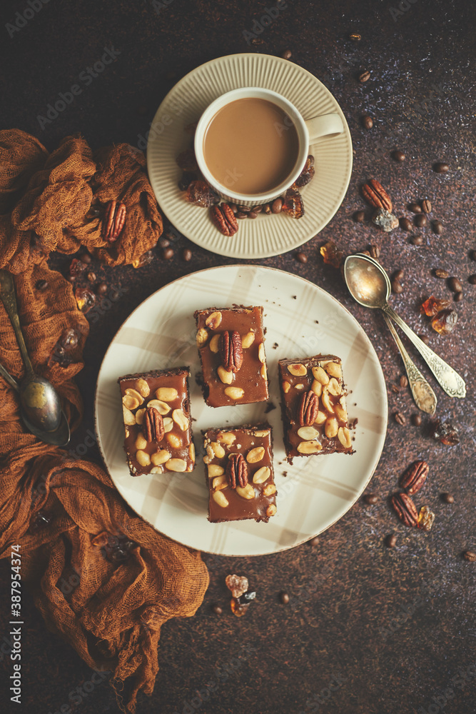 Chocolate cake with caramel frosting, pecans and hot coffee, on rustic background. Freshly baked - obrazy, fototapety, plakaty 