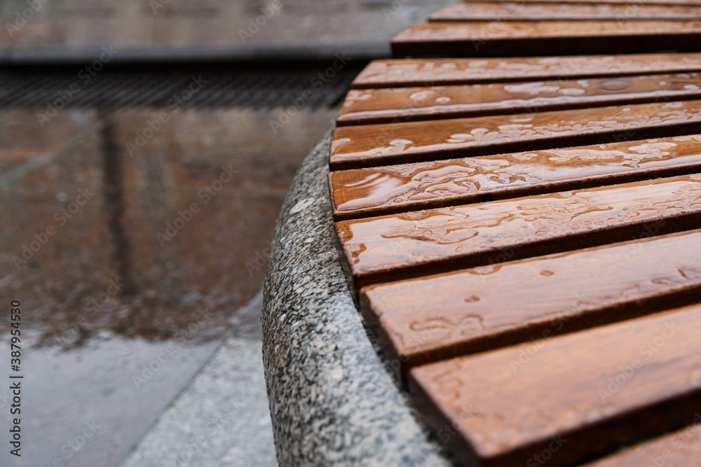 One of the circle benches on the Griboyedov channel embankment in Saint Petersburg on a rainy autumn day in October. Wet wooden planks are laid on a granite pedestal. Copy space