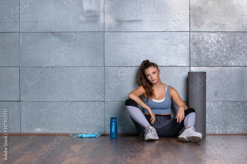 Young fit woman in leggings sitting on the floor with training equipment