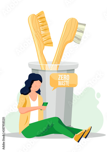 The girl sits on the floor with a smartphone in her hands and writes sms or sends an email. Natural organic wooden toothbrushes in a glass beaker. Zero waste, eco friendy equipment for oral hygiene