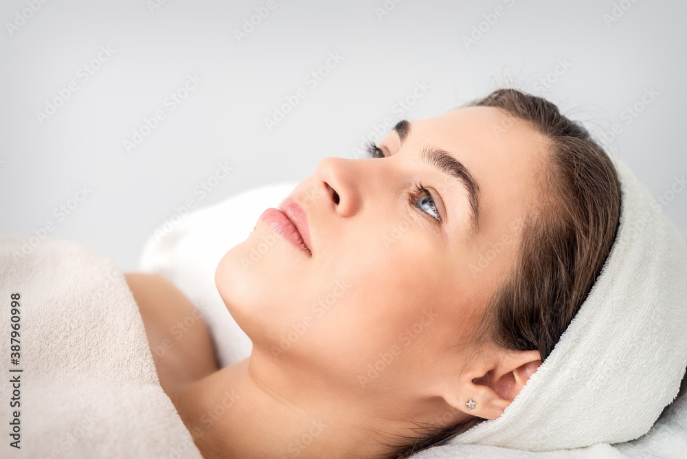 Side view portrait of pensive young woman lying on beautician table while waiting for cosmetic procedure in beauty salon Side view portrait of pensive young woman lying on beautician table while waiting for cosmetic procedure in beauty salon