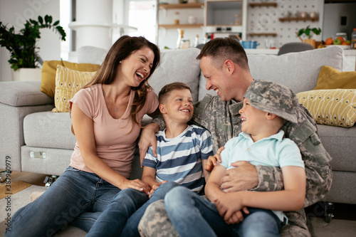 Happy soldier sitting on the floor with his family. Soldier and his wife enjoying at home with children...