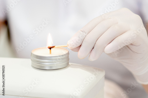 Manicure master in white gloves lighting candle with match in nail salon