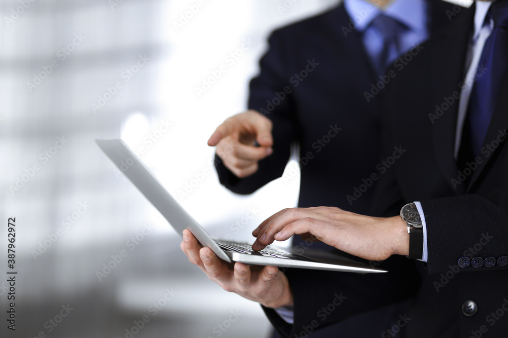 Business people discussing a presentation at meeting, standing in a modern office. Unknown businessman with a colleague search for some information at the laptop, lawyers at negotiation. Teamwork and Business people discussing a presentation at meeting, standing in a modern office. Unknown businessman with a colleague search for some information at the laptop, lawyers at negotiation. Teamwork and