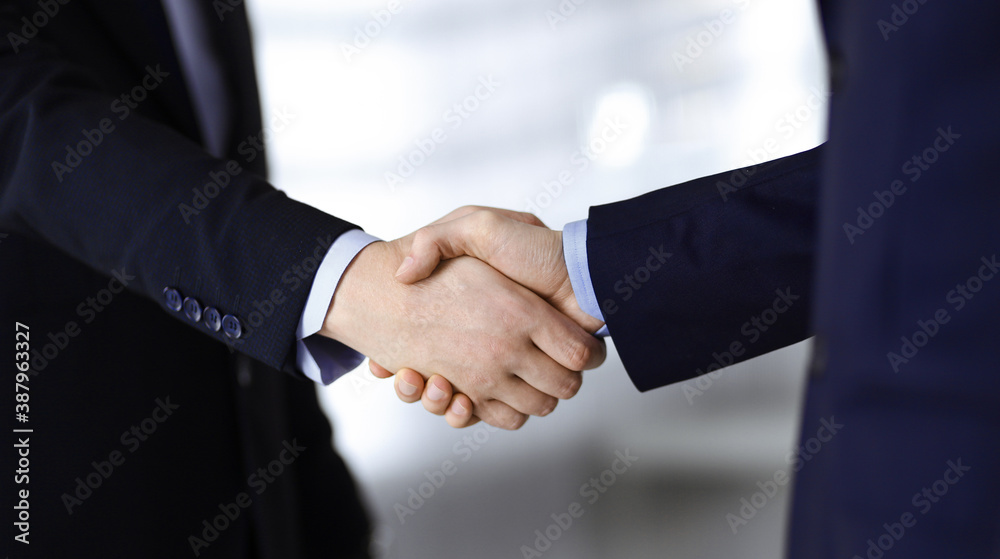 Business people shaking hands, close-up. Group of unknown businessmen standing in a modern office. Teamwork, partnership and handshake concept