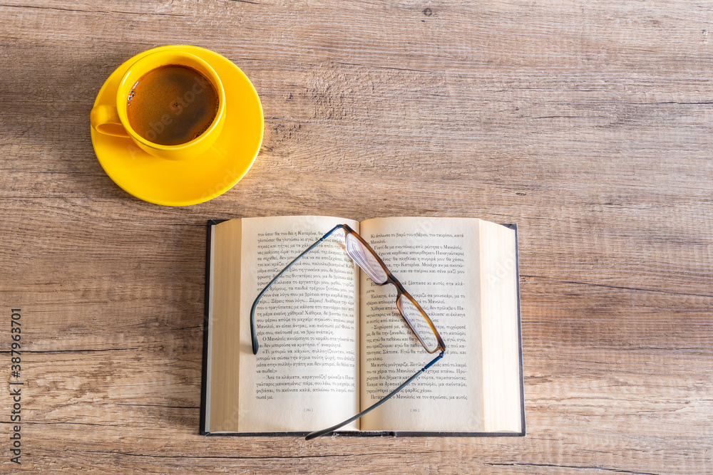 An open book with glasses and a yelloow cup of coffee
